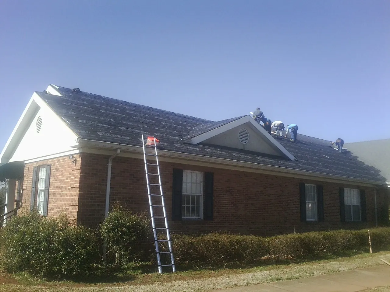 Crew tearing shingles off a brick ranch roof with a ladder set — Metal Roof Repair work by our crew in South Walpole