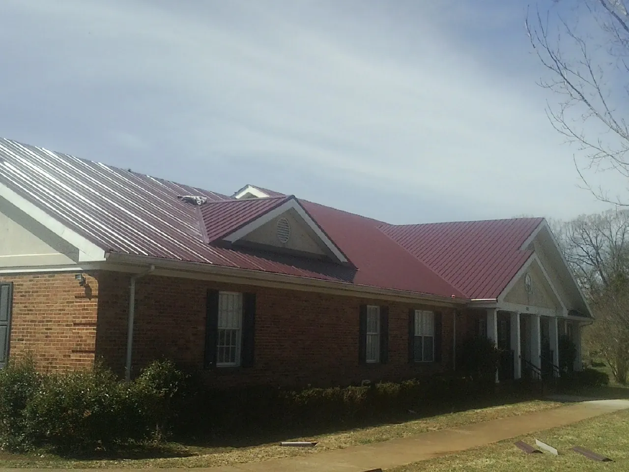 Red metal roof with gabled entries on a long brick building, from a Hail Damage Roof Repair job in South Walpole