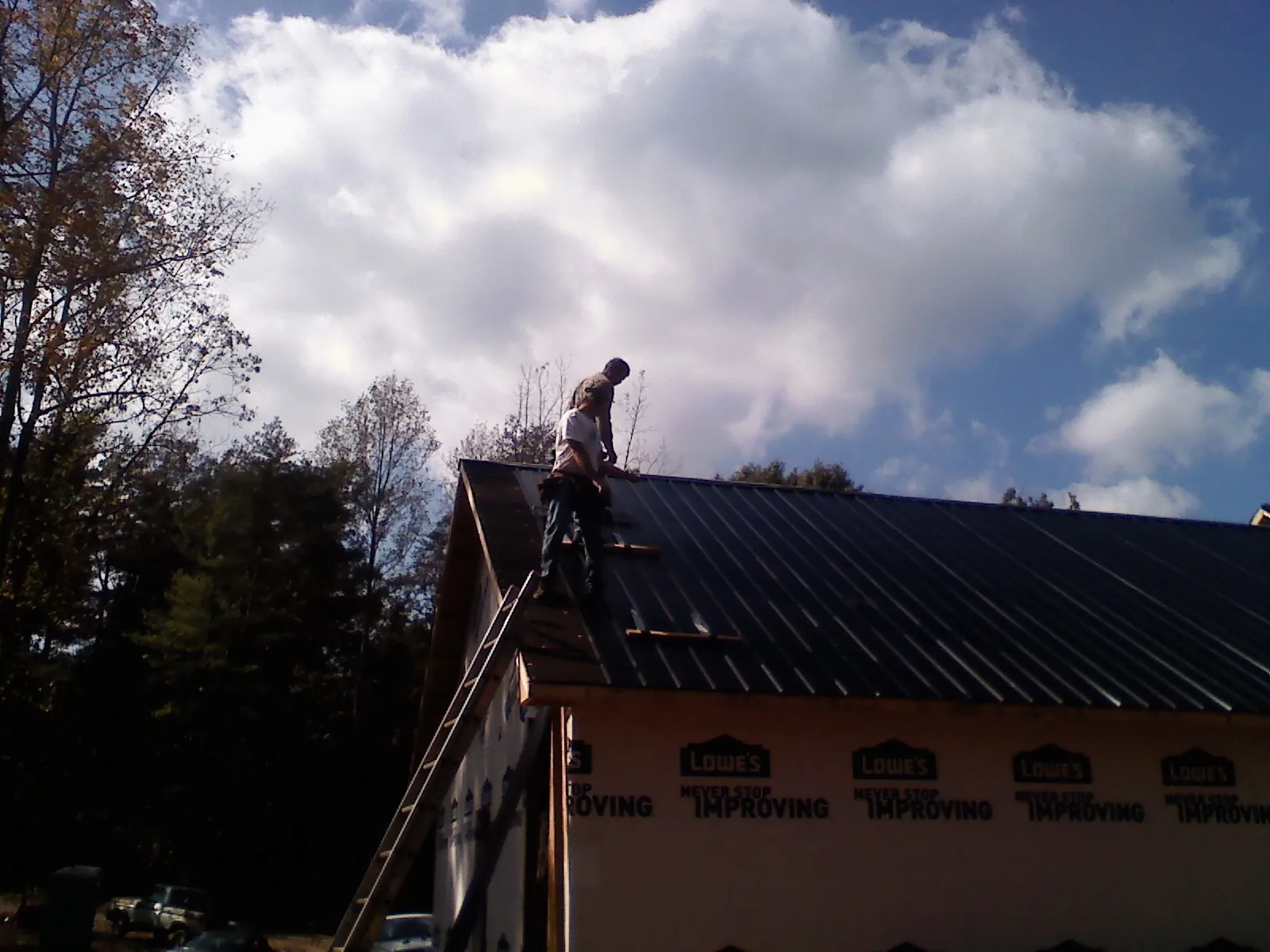 Roofer fastening dark metal panels high against a cloudy sky, from a Roof Inspection job in South Walpole