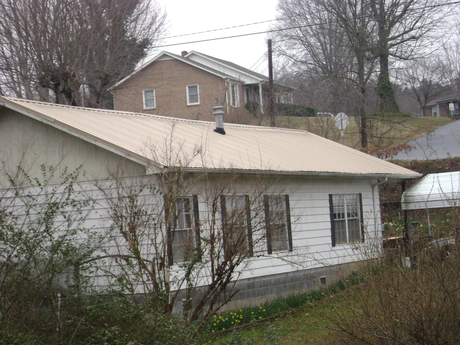 Tan metal roof on a white sided house set into a hillside — Commercial Roofing by Roofing Brothers in South Walpole